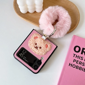 Detail of pink Z Flip case with cute bear embroidery and plush ring on a wooden tray