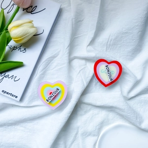 Detail of heart-shaped rotating phone grip with 3D Bonjour text on a white fabric background