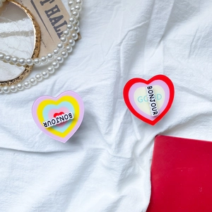 Close-up of heart-shaped acrylic phone grip with Bonjour text on a stylish background