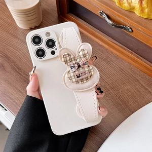 White iPhone case with fabric wrist strap and plush bunny charm on wooden background