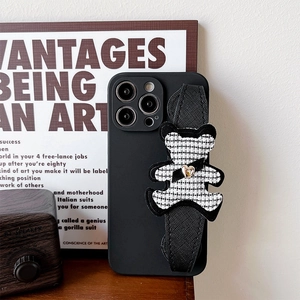 Detail of black iPhone case featuring a houndstooth bear wrist strap and gold heart