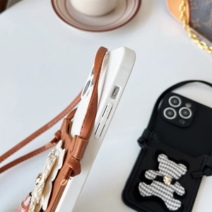 Detail of checkered bear doll and leather shoulder strap on protective iPhone case