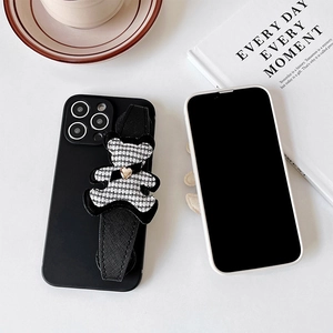 Detail view of black iPhone case featuring a houndstooth bear charm and wrist strap
