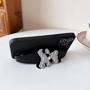 Detail of knitted houndstooth bear strap with golden heart on black leather phone case