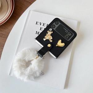 Detail of Galaxy Z Flip4 case with gold bear heart charms and a white faux fur pompom