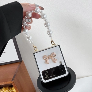 Detail of white grid Z Flip case featuring pearl bow decoration and handheld pearl chain