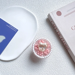 Detail of pink cream cake phone grip with cute resin bear and bow on ceramic plate