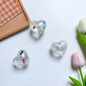 Detailed view of clear heart resin phone grips with floral and bow tie ornaments