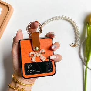 Détail d'étui en cuir orange avec nœud en perles et anneau en strass dorés élégant