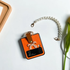 Détail de la coque en cuir orange avec nœud en perles et anneau doré pour Z Flip 6