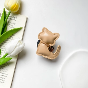Detail of leather cat phone grip with stitching and golden lucky charm on book