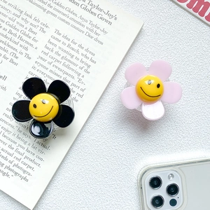 Close-up of black and pink flower phone socket grips with smiley face on white leather