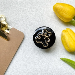Detailansicht einer schwarzen Handyhalterung mit goldenem Bär-Umriss auf weißem Tisch