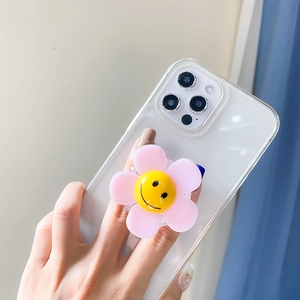 Close-up of a pink 3D flower phone grip with a yellow smiley face on a clear case