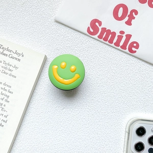 Detail of expandable green phone grip with 3D yellow smiley face on desk