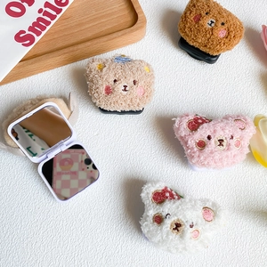 Plush teddy bear phone socket grips and square flip mirror on white leather surface