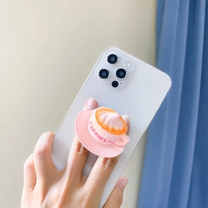 Pink cappuccino coffee cup shaped phone grip stand held against a colorful interior