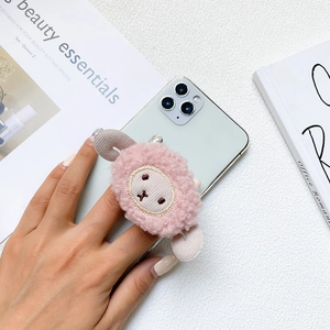 Detail showing plush pink lamb phone grip with cute embroidery on a silver smartphone