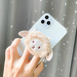 Close-up of cute plush lamb phone grip with soft beige wool texture and embroidered face