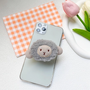 Close-up of cute plush sheep phone grip with built-in mirror on a green smartphone