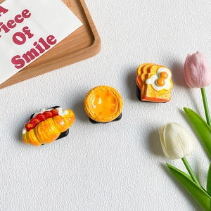 Detail shot of croissant and egg tart food shaped phone grips on a wooden tray