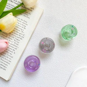 Set of three transparent donut-style phone grips in purple, grey, and green with glitter