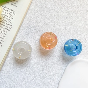 Detail of transparent doughnut phone grips with colorful glitters on minimalist white desk