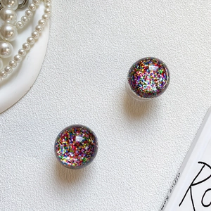 Macro shot of colorful glitter resin ball earrings on a clean minimalist desk surface
