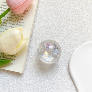 Detail of a round clear resin phone grip with colorful star and shell sequins in sunlight