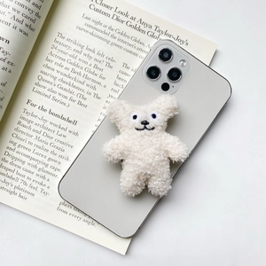 Close-up of white plush bear phone grip on silver phone with soft sherpa texture