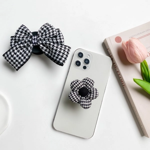 Detail view of houndstooth fabric phone grip with bow and flower patterns on white phone