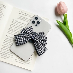 Detail of fabric bow phone grip with black and white houndstooth pattern on white smartphone