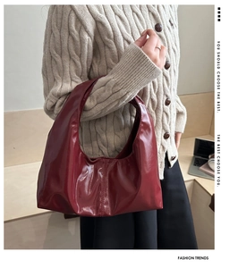 Detail of a dark red glossy hobo bag worn with a cozy beige knit sweater