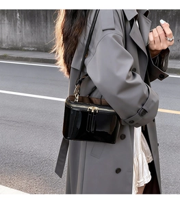 Close-up of black patent leather crossbody box bag with gold zipper and shoulder strap