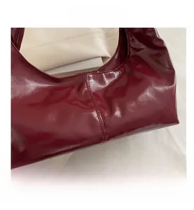 Detail shot of glossy burgundy patent leather with vertical stitching on underarm bag