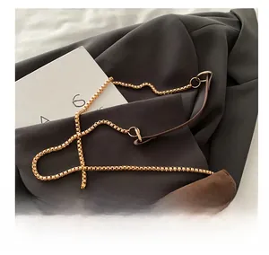 Gros plan d'un sac enveloppe en daim marron avec chaîne à billes dorée sur une veste