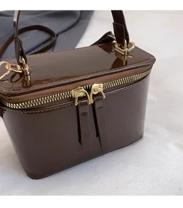 Detail of a brown patent leather box bag with dual gold zippers and metallic hooks