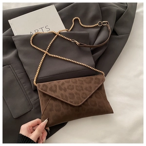 Détail de la pochette léopard en daim avec fine chaîne dorée sur fond de tissu