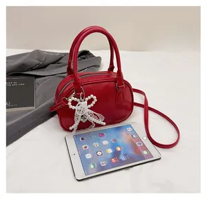 Detail of red oval leather crossbody bag with pearl bow charm and size reference