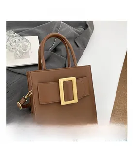 Detail of a brown leather crossbody bag with a large square gold buckle in an urban setting