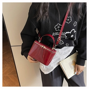 Model showing a red patent leather box bag with handle and detachable shoulder strap