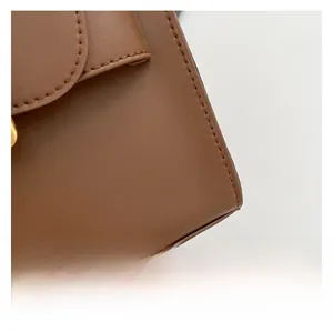 Detail shot of brown leather texture with fine stitching and gold metal buckle on a square bag
