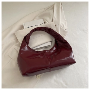 Close-up of a burgundy patent leather hobo bag with sleek stitching on a beige blazer