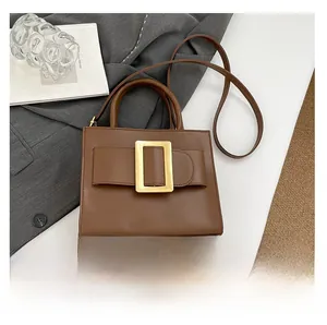 Detailed view of brown leather square crossbody bag with large gold buckle in a stylish setup