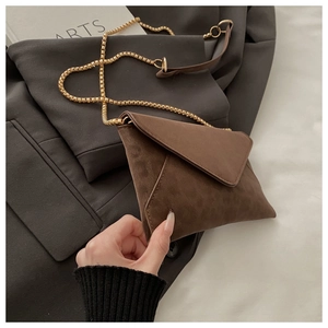 Détail d'un sac enveloppe marron en daim avec chaîne dorée sur une veste chic