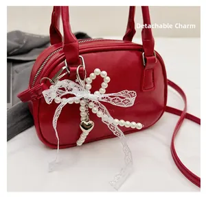 Close-up of red PU leather handbag featuring a detachable pearl and lace bow pendant