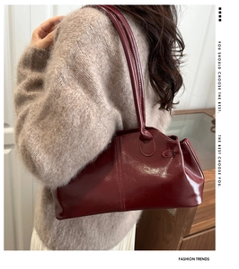 Detail of burgundy patent leather underarm bag with sleek metallic buckle and shoulder strap