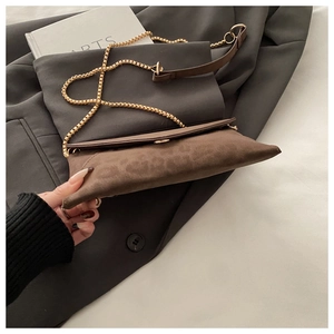 Détail de la pochette en daim marron avec chaîne dorée sur une veste grise