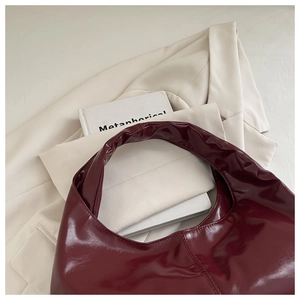 Detail of dark red glossy patent leather underarm bag on a stylish cream blazer
