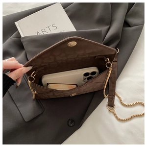 Détail d'un sac enveloppe marron embossé léopard avec chaîne dorée sur un blazer